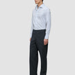 En man bär en blå randig skjorta av modellen Elevated Shirt Slim Classic och kolgrå byxor medan han står i profil.