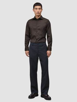 En man klädd i en mörkbrun Elevated Shirt Slim, instoppad i grå byxor och mörka läderskor.