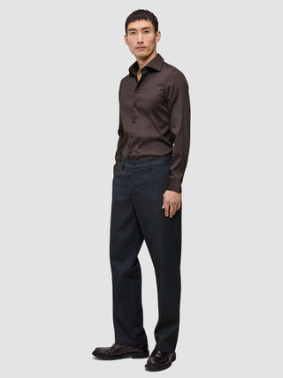 En man klädd i en mörkbrun Elevated Shirt Slim och kolgrå byxor.