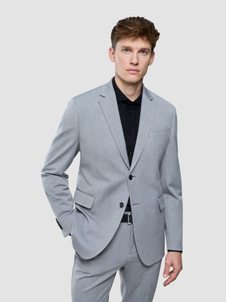 En man klädd i en Essential Blazer Regular Ash Twill över en svart skjorta med knappar.