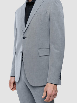 En person som bär en Essential Blazer Regular Ash Twill över en svart skjorta med krage i en ren, skandinavisk design.