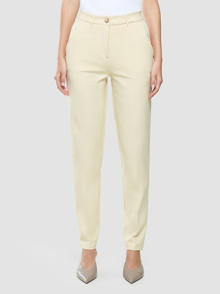 En person som bär byxor av modellen ”Women Essential Pants Tapered” i färgen ”Misty Yellow” och högklackade skor med spetsig tå.