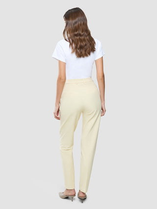 En kvinna sedd bakifrån, klädd i en vit t-shirt, ett par Women Essential Pants Tapered i färgen Misty Yellow och mules.