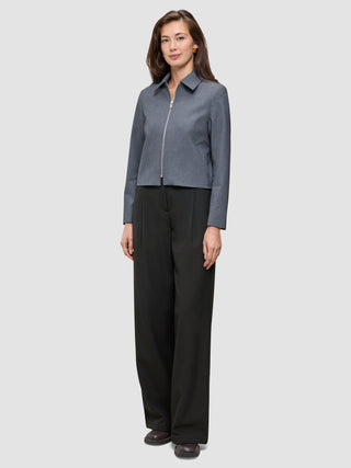 En kvinna klädd i en Essential Short Zip Jacket i mörkgrå melange och svarta byxor i minimalistisk skandinavisk design.