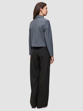 En kvinna sedd bakifrån, klädd i en Essential Short Zip Jacket i mörkgrå melange och svarta byxor.
