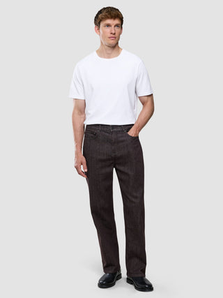 En man klädd i en vit t-shirt och ett par mörkbruna Marco Jeans står framför en enfärgad bakgrund.