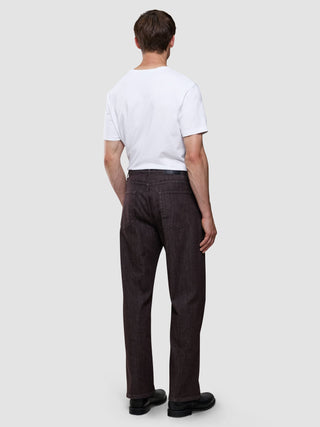En man sedd bakifrån, klädd i en vit t-shirt och ett par Marco Jeans i mörkbrunt.