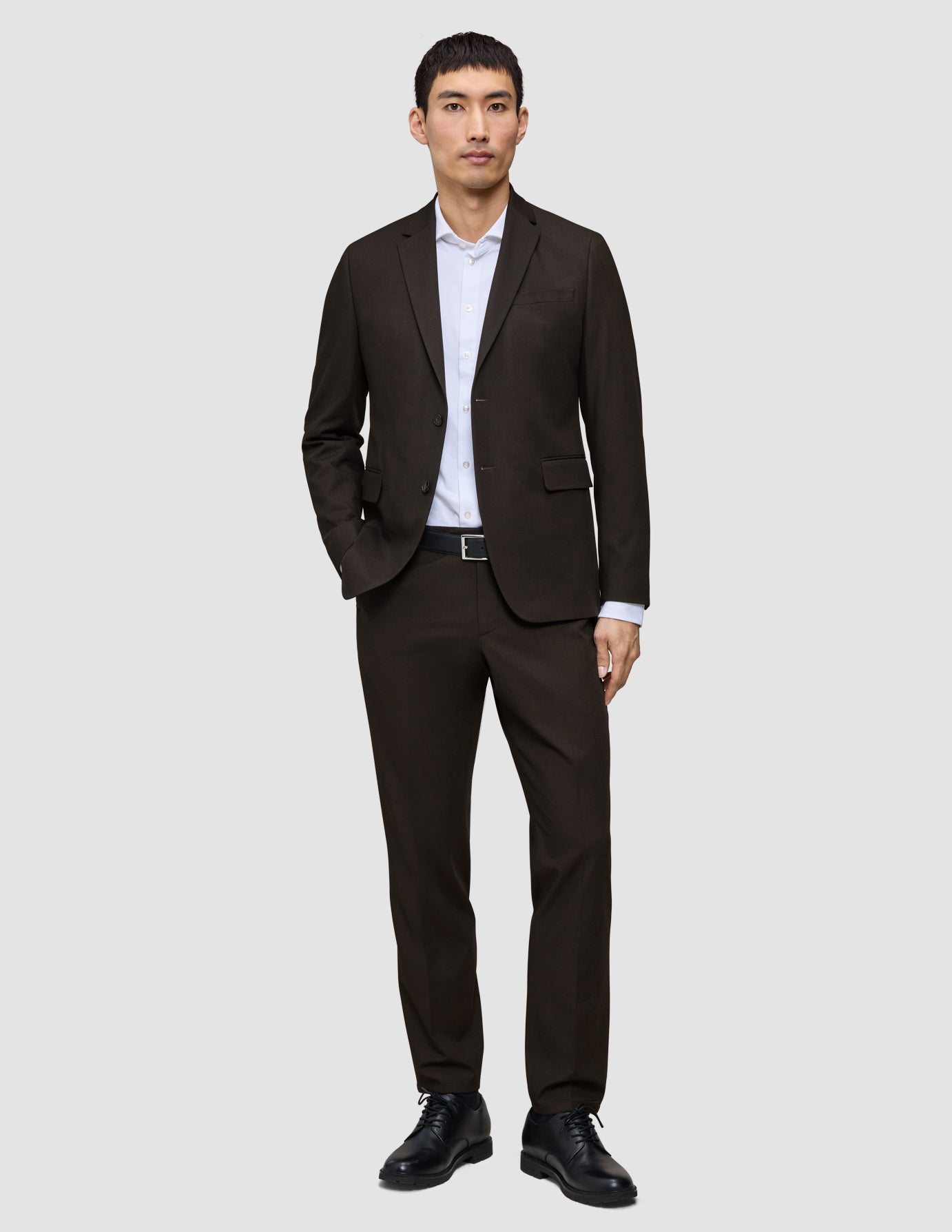En man klädd i en mörkbrun Motion Blazer Regular Cognac, en vit skjorta och svarta läderskor.