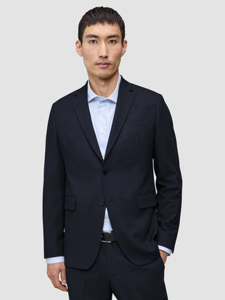 En man klädd i en Motion Blazer Regular i färgen Midnight Blue över en ljusblå, randig skjorta med knappar.