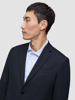 En man i en Motion Blazer Regular i färgen Midnight Blue, som han bär över en ljusblå randig skjorta med knappar.