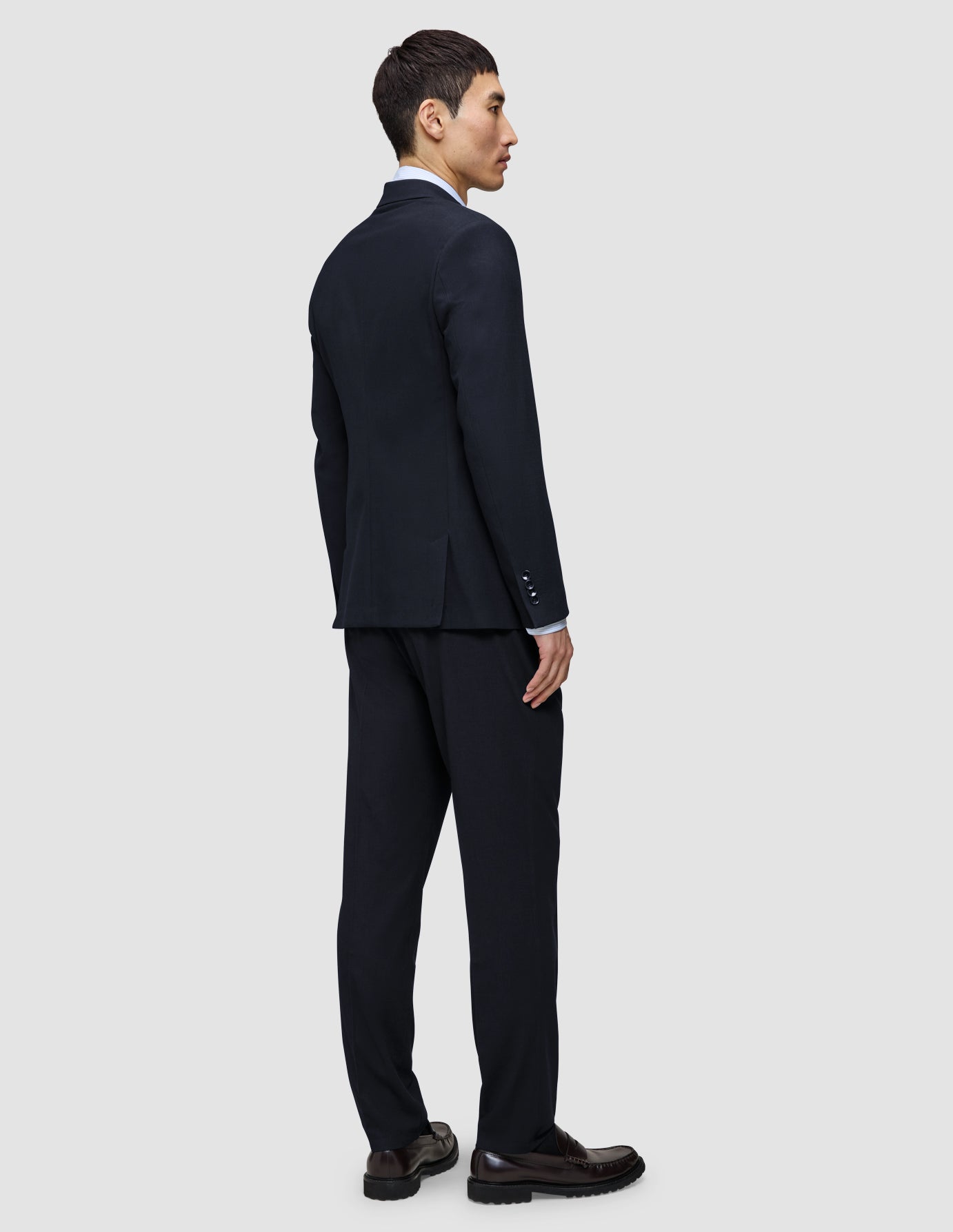 En man sedd bakifrån, klädd i en Motion Blazer Regular i färgen Midnight Blue, matchande byxor, en ljus skjorta och mörka loafers.