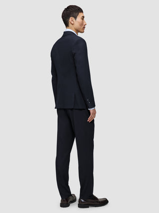 En man sedd bakifrån, klädd i en Motion Blazer Regular i färgen Midnight Blue, matchande byxor, en ljus skjorta och mörka loafers.