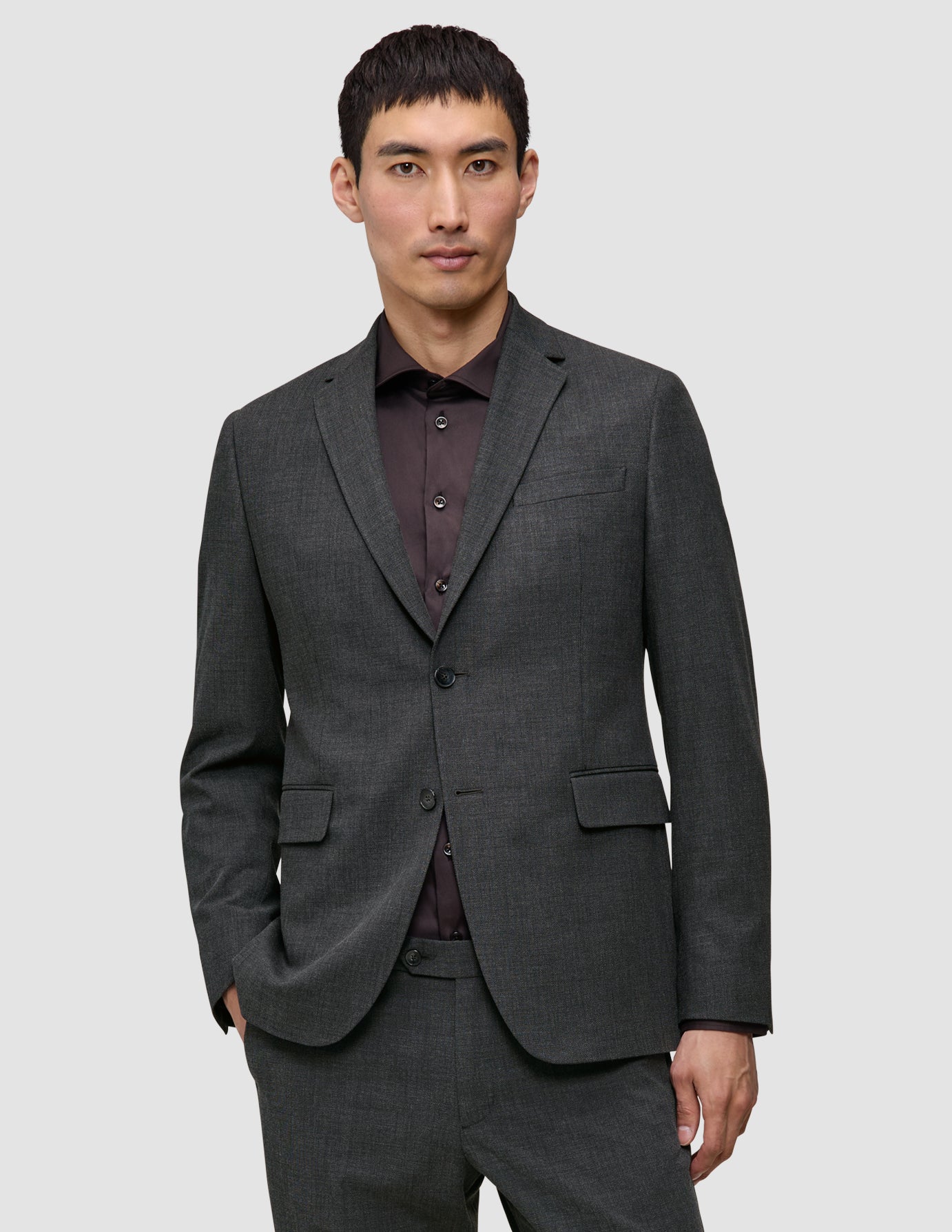 En man klädd i en Motion Blazer Regular i färgen Pepper Grey över en mörk skjorta med knappar.