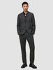En man klädd i en kostym av märket Motion Blazer i modell Regular i färgen Pepper Grey, tillsammans med en mörk skjorta med knappar och loafers.