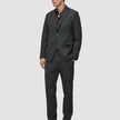 En man bär en Motion Blazer Regular i färgen Pepper Grey och matchande byxor över en mörk skjorta med knappar och loafers.