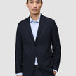 En man bär en Motion Blazer Slim i färgen Midnight Blue över en ljusblå, randig skjorta med knappar.