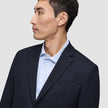 En man klädd i en Motion Blazer Slim i färgen Midnight Blue över en ljusblå randig skjorta.