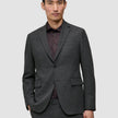 En man klädd i en Motion Blazer Slim i färgen Pepper Grey över en mörklila skjorta med knappar.