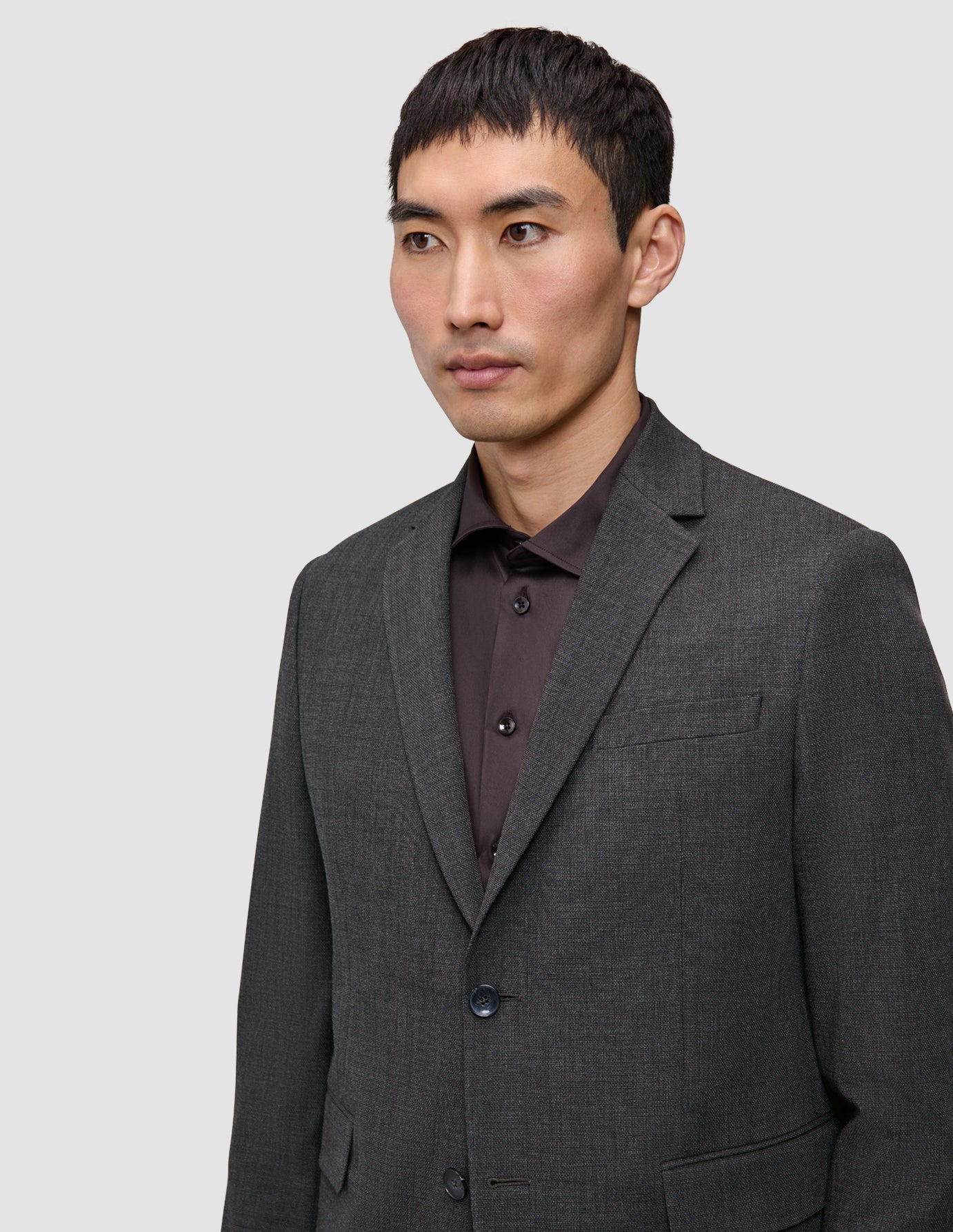 En man klädd i en Motion Blazer Slim i färgen Pepper Grey över en mörk skjorta med knappar.