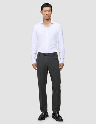 En man i en vit skjorta och byxor av modellen Motion Suit Pants Regular Pepper Grey, kombinerade med svarta loafers.