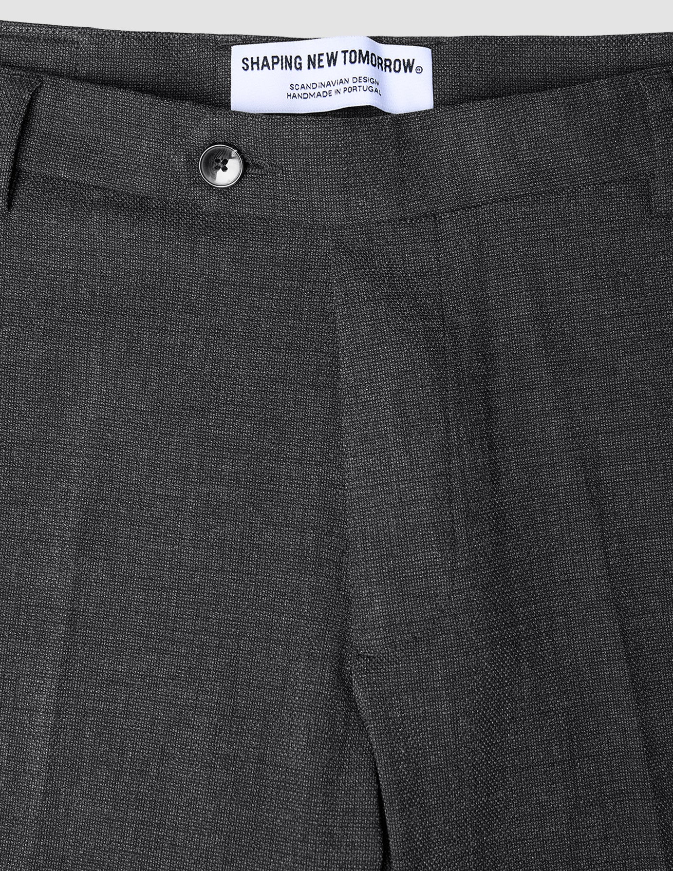 Närbild på de kolgrå Motion Suit-byxorna i modell Slim Pepper Grey, med knappstängning och en inbyggd märkesetikett.