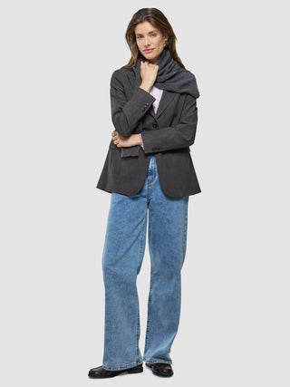 En kvinna klädd i en Women Nara Blazer Cool Brown, en ljusrosa skjorta, en mörk halsduk och blå jeans med vida ben.