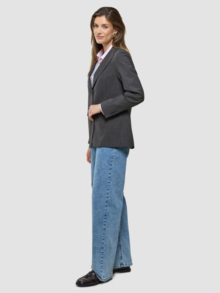 En kvinna klädd i en Women Nara Blazer Cool Brown, en ljusrosa skjorta och blå jeans med vida ben.