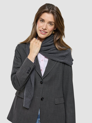 En leende kvinna klädd i en Women Nara Blazer Cool Brown, en ljusrosa skjorta och en mörkgrå halsduk.