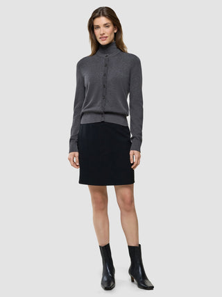En kvinna klädd i en ”Women Quinn Crewneck Cardigan Cool Brown”, svart kjol och svarta ankelstövlar, som visar upp skandinavisk design.