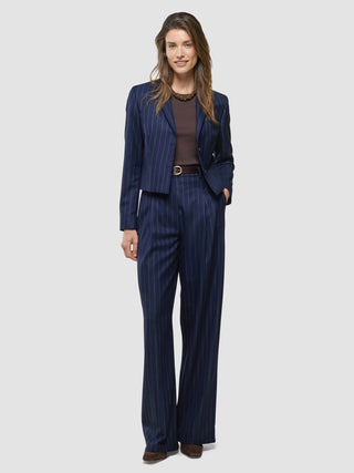 En kvinna bär en Raina Short Blazer i färgen Night Sky med smala ränder och matchande byxor med vida ben över en brun topp.