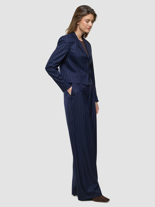 En kvinna klädd i en kort damblazer av modellen ”Raina” i färgen ”Night Sky Pinstripe” och matchande byxor med vid benvidd.
