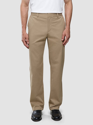 En person som bär ett par Refine-bomullsbyxor i modell Relaxed Fit i färgen Sand, tillsammans med en vit t-shirt och svarta kostymskor.