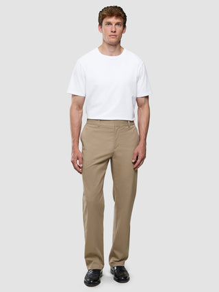 En man klädd i en vit T-shirt med rund hals, Refine-bomullsbyxor i avslappnad passform i färgen ”Sand” samt svarta finskor.
