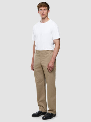 En man klädd i en vit t-shirt och ett par Refine-bomullsbyxor i avslappnad passform i färgen Sand.