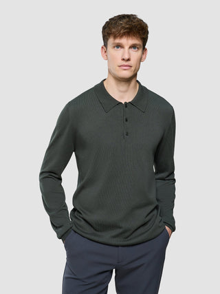 En man klädd i en Seamless Core Knit Long Sleeve Polo Green Night i minimalistisk skandinavisk design.