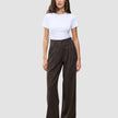 En person bär en vit t-shirt och byxorna Serene Pants Wide Walnut Herringbone: bruna byxor med hög midja och vida ben.