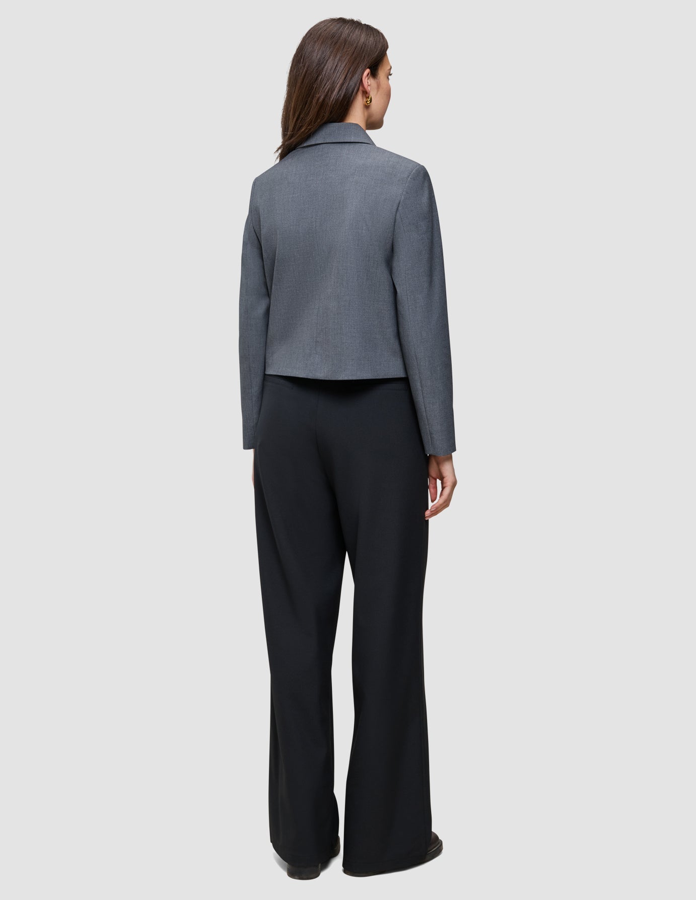 En person sedd bakifrån, klädd i en grå kavaj och svarta Serene Pants Wide Black med hög midja.