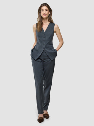 En kvinna klädd i en ”Women’s Skye Long Vest Charcoal Melange” och matchande byxor, med händerna i fickorna.