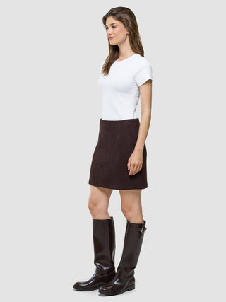 En kvinna klädd i en vit t-shirt, en kort kjol från Women Sorae i färgen Espresso och knähöga stövlar.