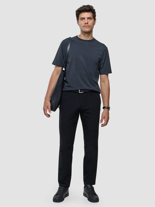 En man i en Supima-T-shirt i Box Fit-modell i mörkgrått och svarta byxor bär en svart tygväska med skandinavisk design.