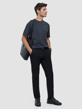 En man i en Supima-T-shirt i modell Box Fit i färgen Deep Grey och svarta byxor bär en svart tygväska över axeln.