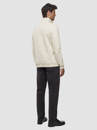 En man sedd bakifrån, klädd i en offwhite tröja med halv dragkedja, mörka jeans och svarta loafers.