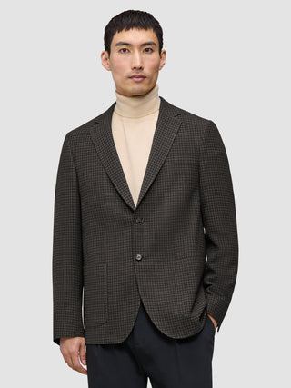 En man klädd i en mörkbrun rutig Timeless-ullblazer i smal passform över en beige polotröja, vilket återspeglar klassisk skandinavisk design.