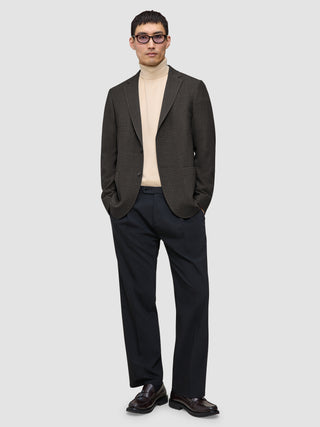 En person som bär en mörkbrun rutig Timeless Wool Blazer Slim över en beige polotröja och mörka byxor.