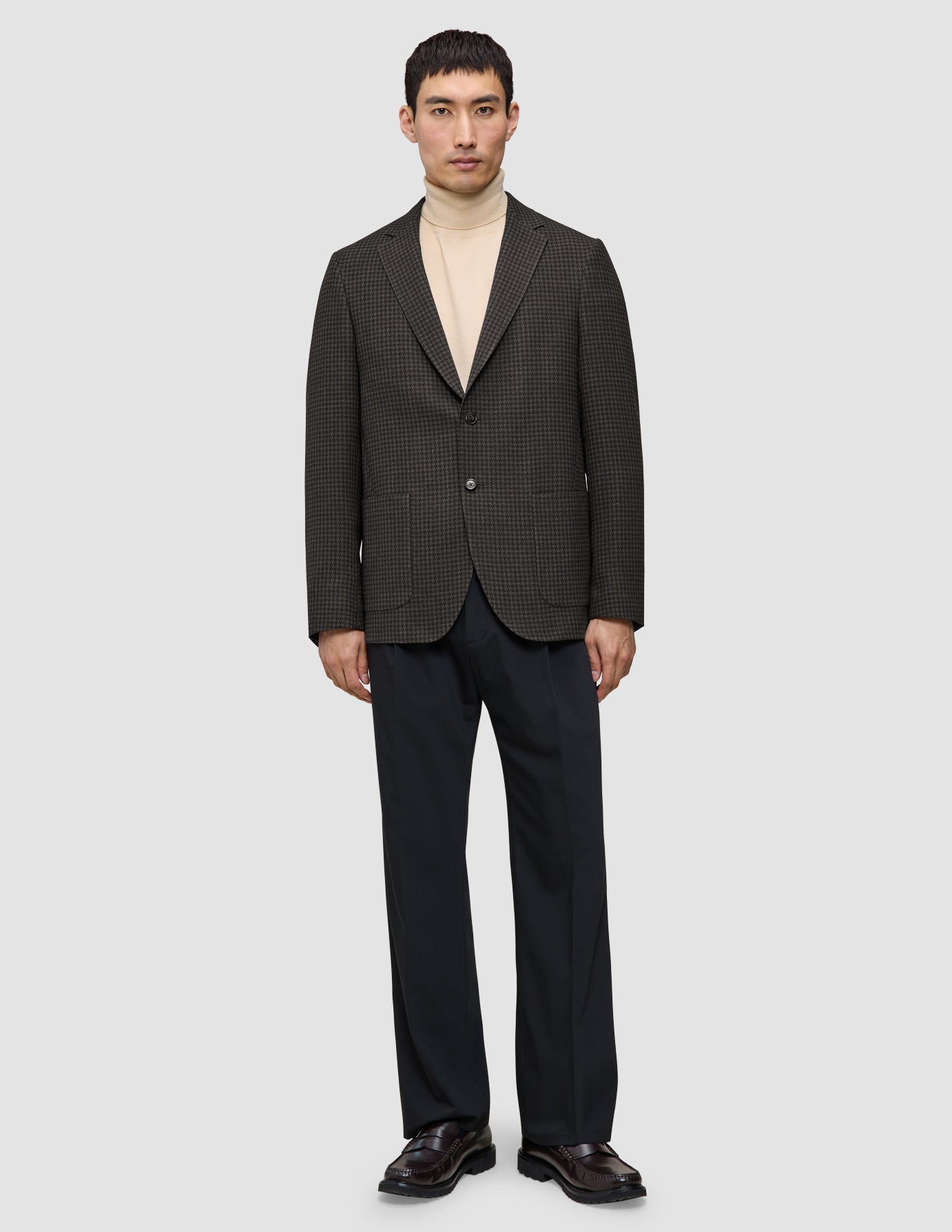En man bär en mörkbrun rutig Timeless Wool Blazer Slim över en krämfärgad polotröja och mörka byxor.