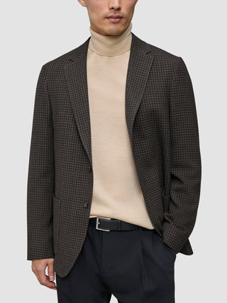 En person som bär en mörkbrun rutig Timeless Wool Blazer Slim över en beige polotröja och svarta byxor.