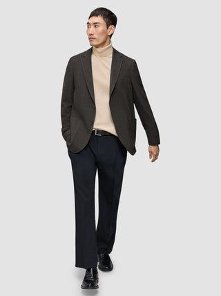 En man klädd i en mörkbrun rutig Timeless-ullblazer i smal passform, en beige polotröja, svarta byxor och loafers.
