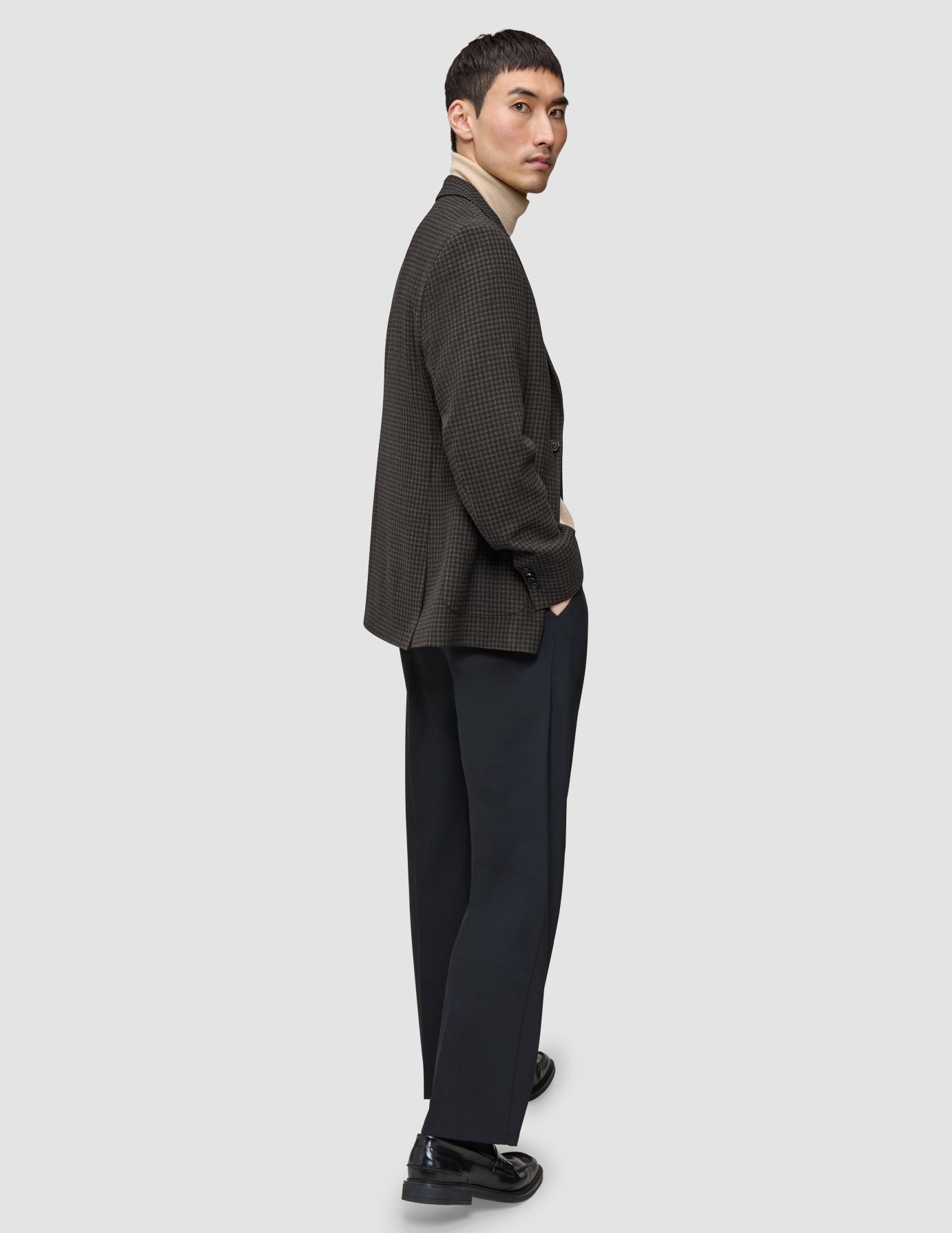 En person klädd i en mörkbrun rutig Timeless Wool Blazer Slim, en beige polotröja och mörka byxor.