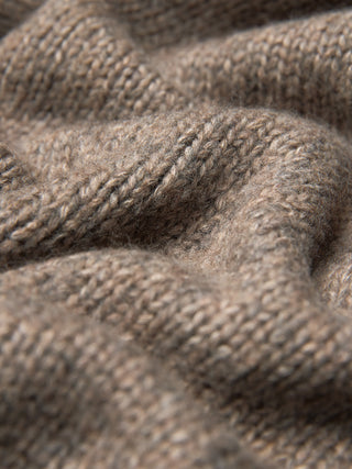 Närbild på en tjock, mjuk stickad damtröja med hög hals i taupe-melange, med en grov, ribbad struktur i taupe.