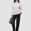 En kvinna klädd i en krämfärgad tröja med hög hals och svarta Women GO2 Pants Straight, som håller en svart handväska.